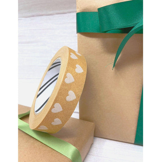 Roll of brown tape with white heart patterns next to a brown paper bag with green ribbon