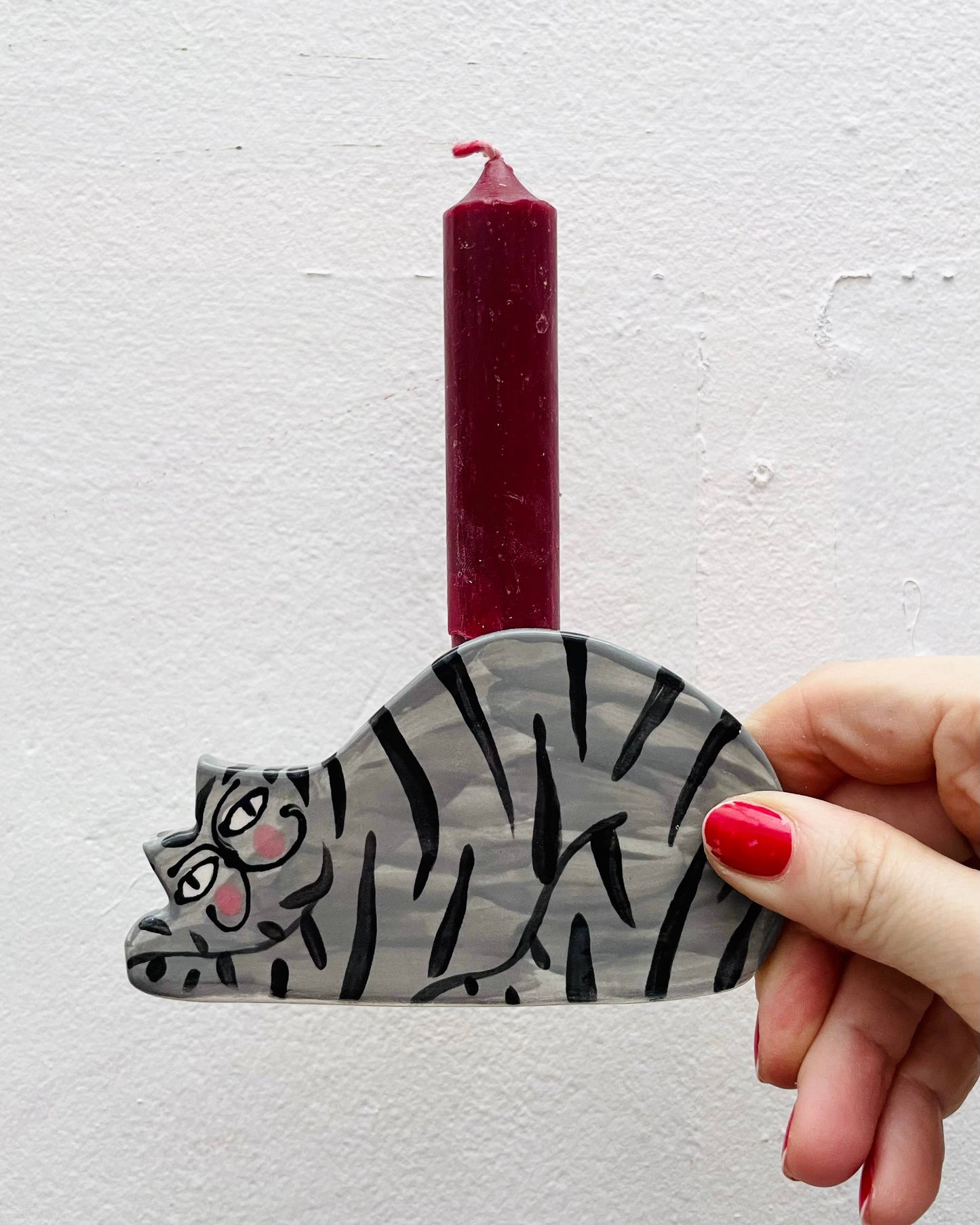 Hand holding a cat-shaped candle holder with a red candle against a light gray background