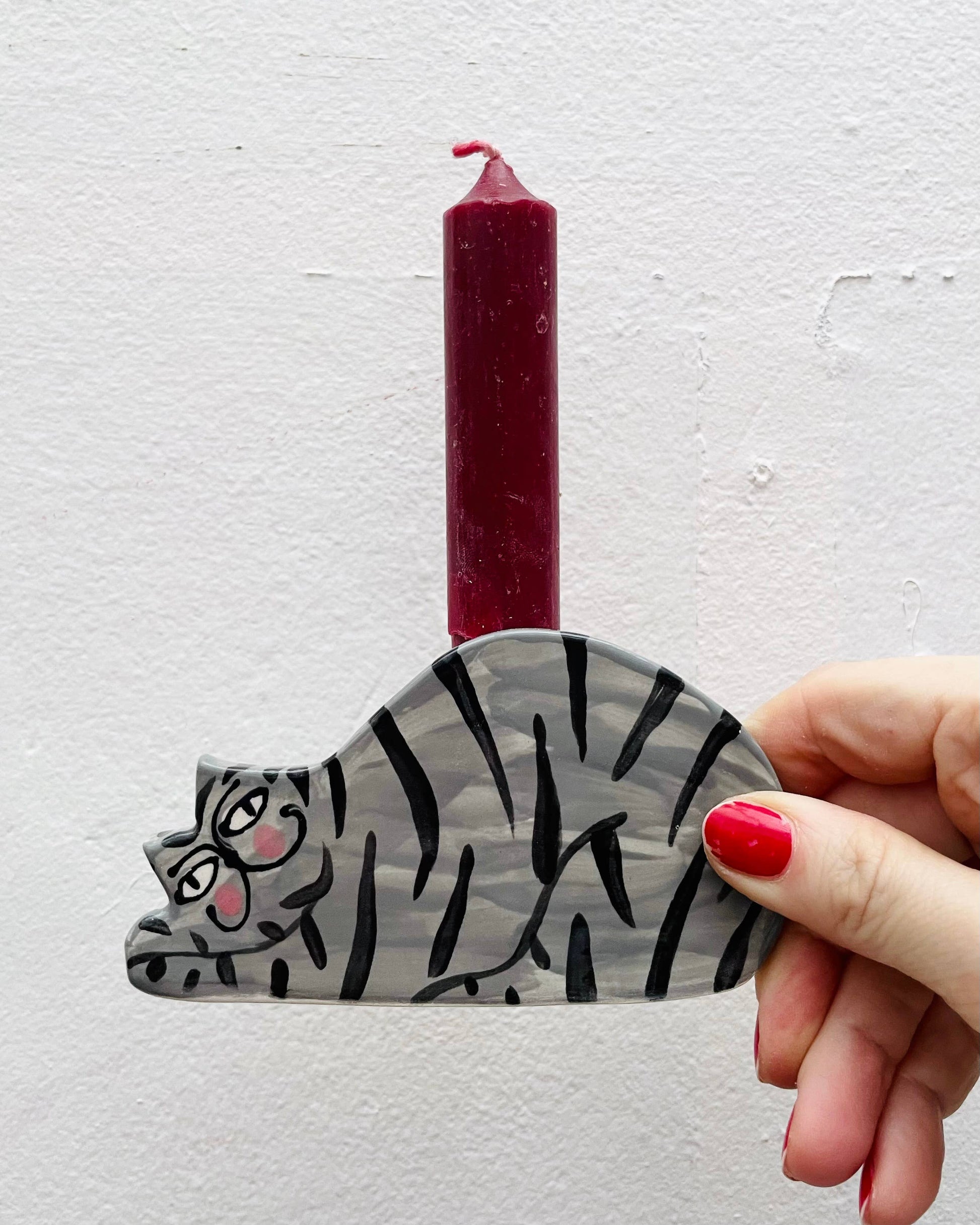 Hand holding a cat-shaped candle holder with a red candle against a light gray background