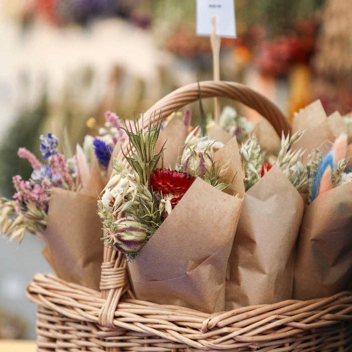 Wicker basket filled with paper-wrapped gifts and flowers on a blurred background