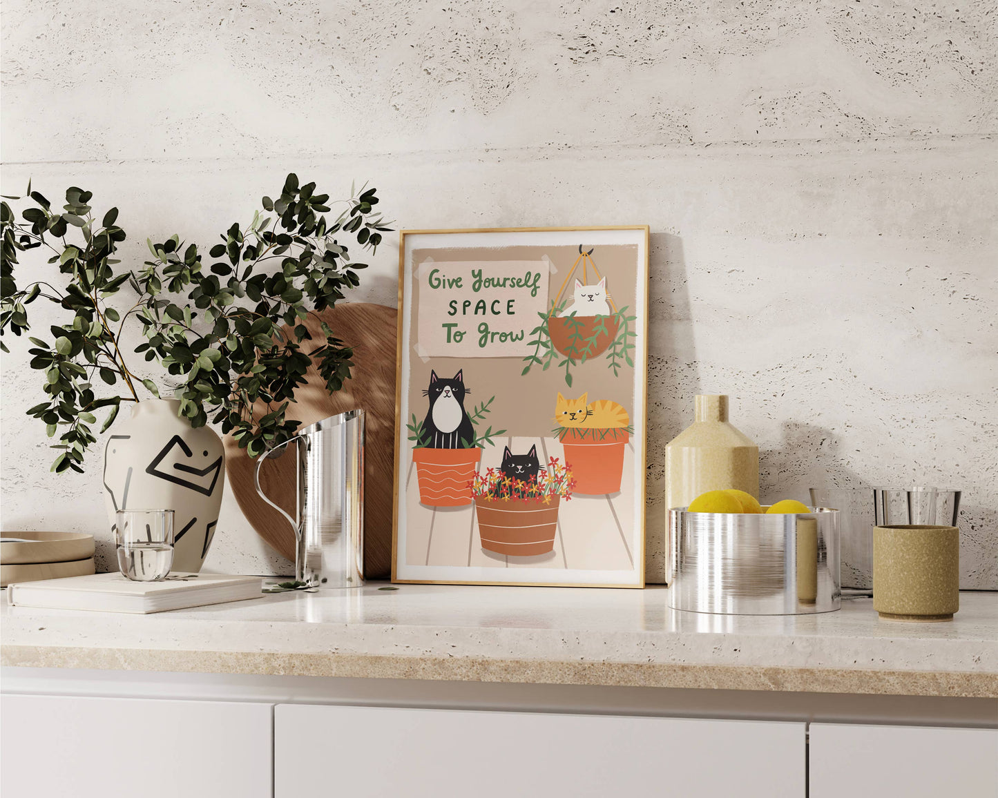 Decorative setup with a framed print, plants, and kitchen items on a countertop.