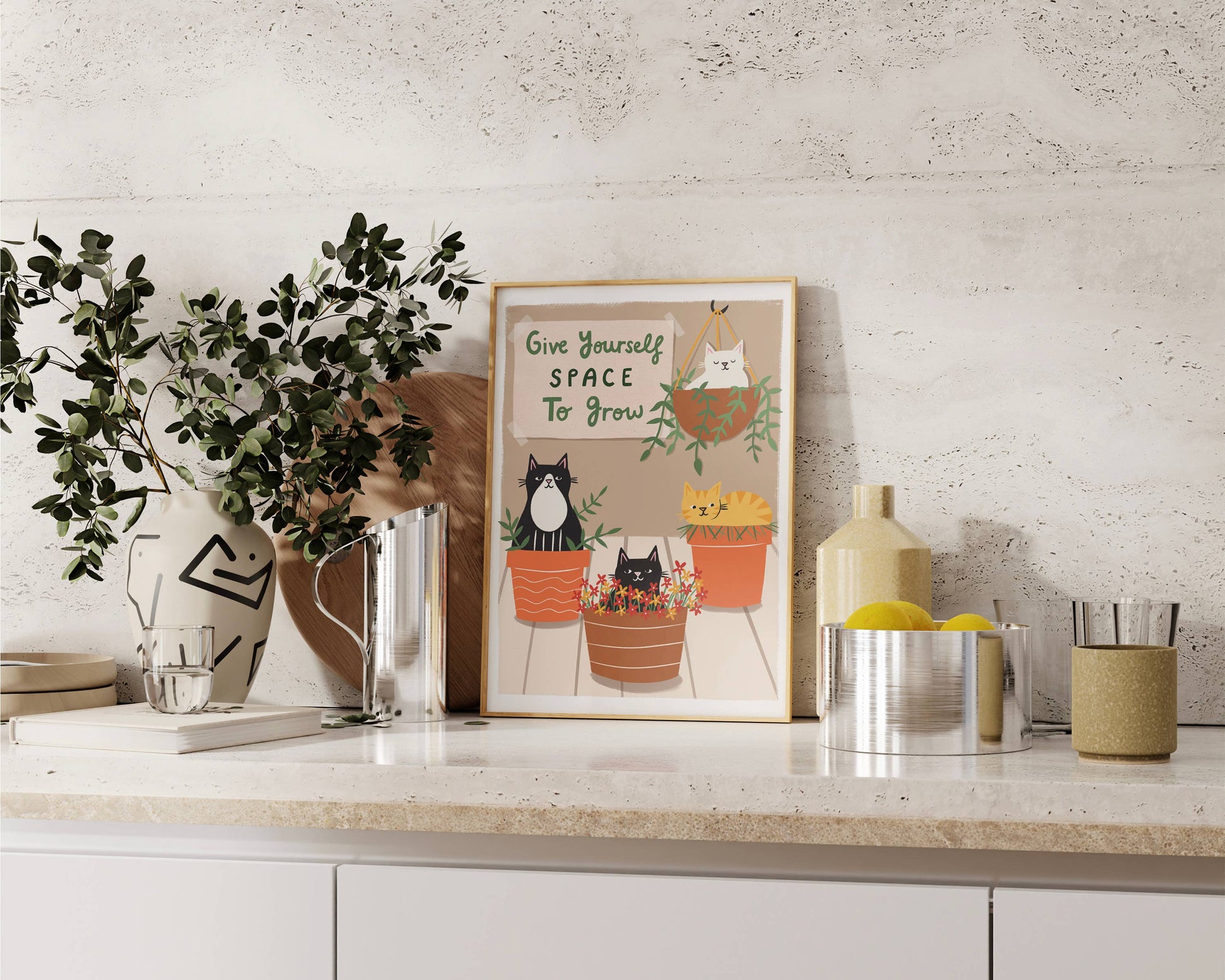 Decorative setup with a framed print, plants, and kitchen items on a countertop.