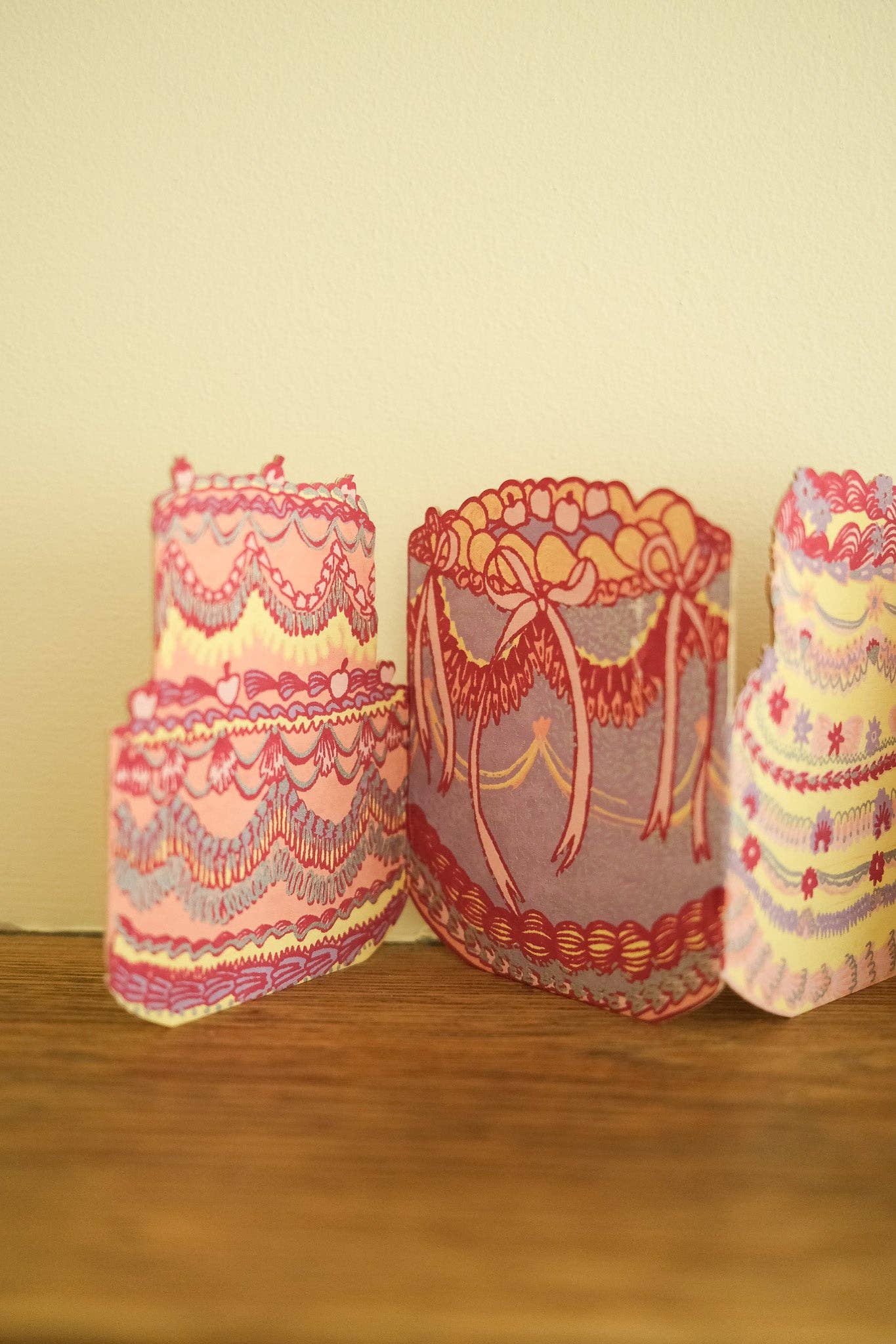 Three decorative candles with lace designs on a wooden surface against a beige wall.