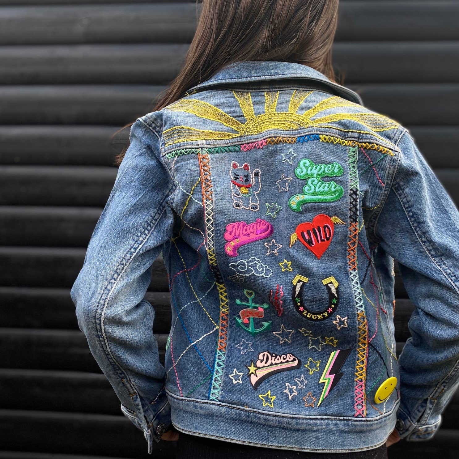 Denim jacket with colorful patches and embroidery on a person against a black background
