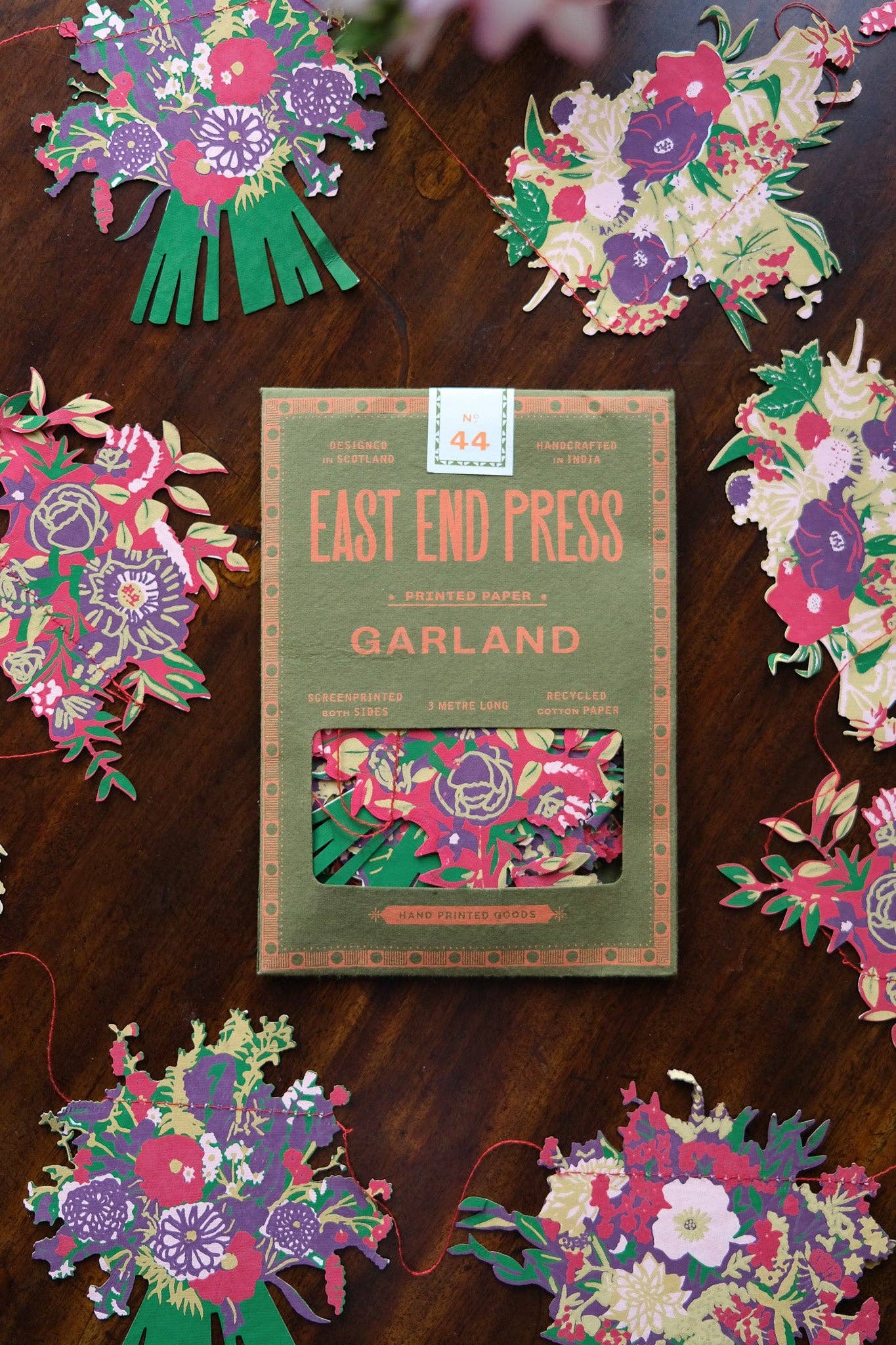 Packaged Garland with East End Press branding on a wooden surface surrounded by decorative paper garlands.