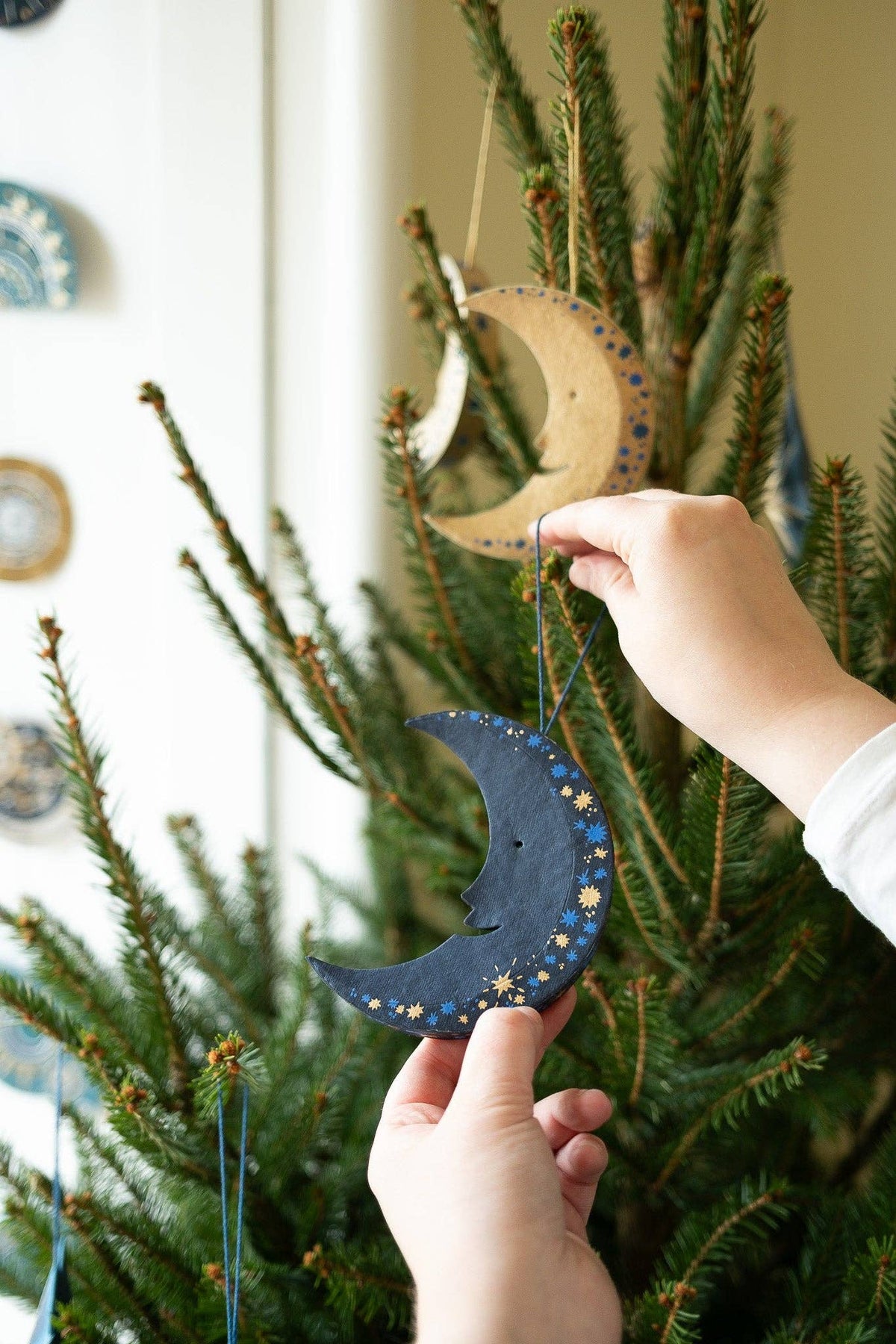 Person holding decorative moon ornaments in front of a Christmas tree