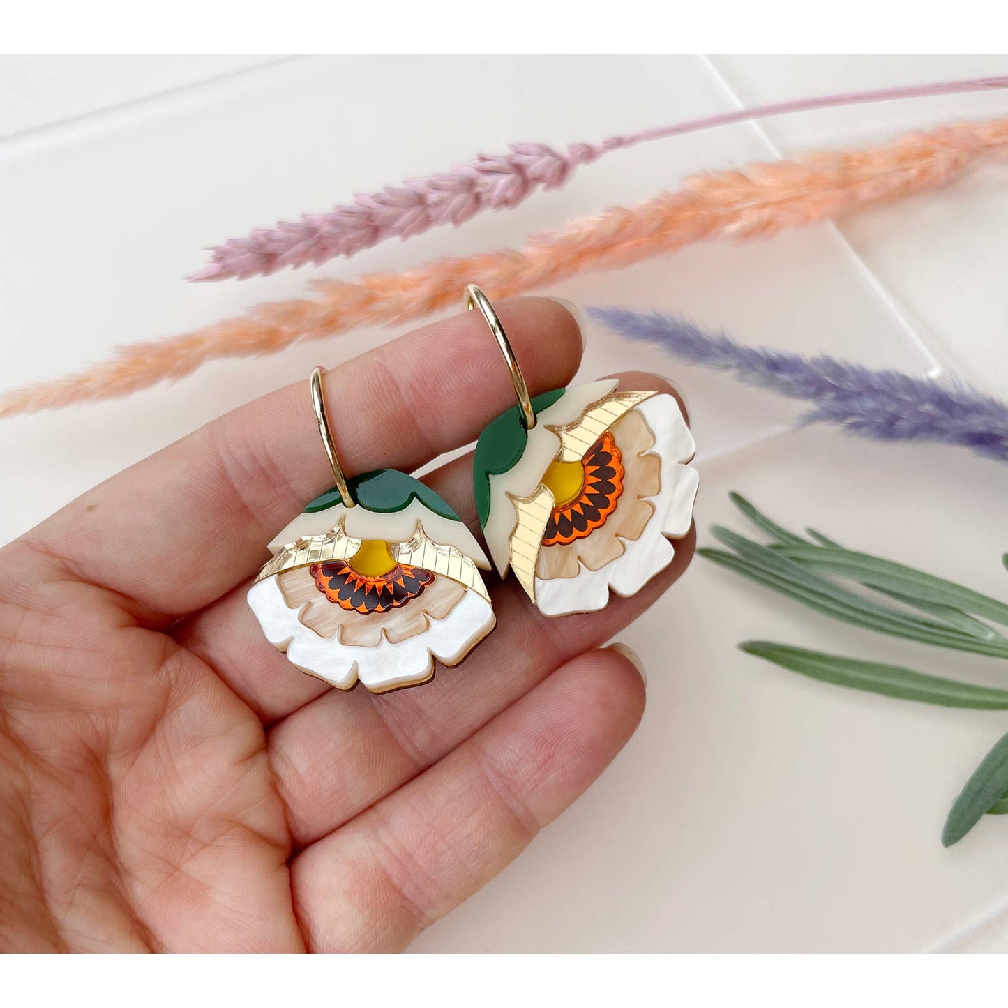 Floral earrings held in a hand with a floral background