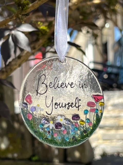 Decorative hanging disc with 'Believe in Yourself' text and colorful flowers, blurred background