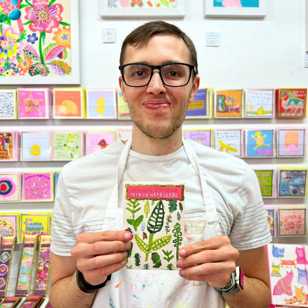 Man holding a colorful card in front of a wall of art cards