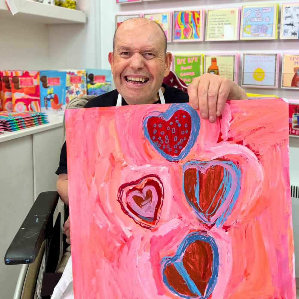 Man holding a painting with heart designs in a store setting