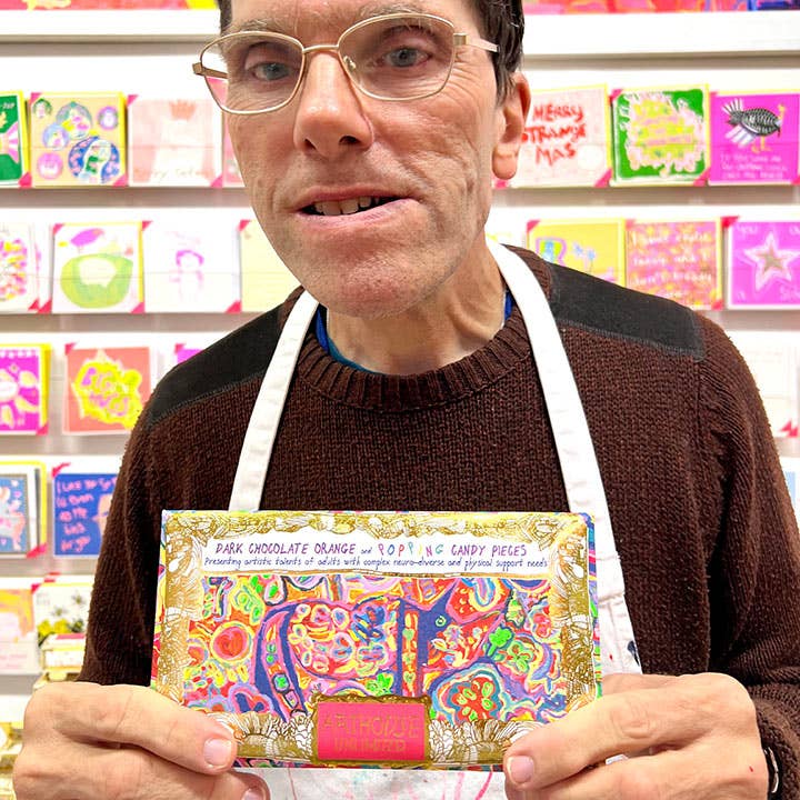 Man holding a colorful chocolate bar in front of a shelf with various items