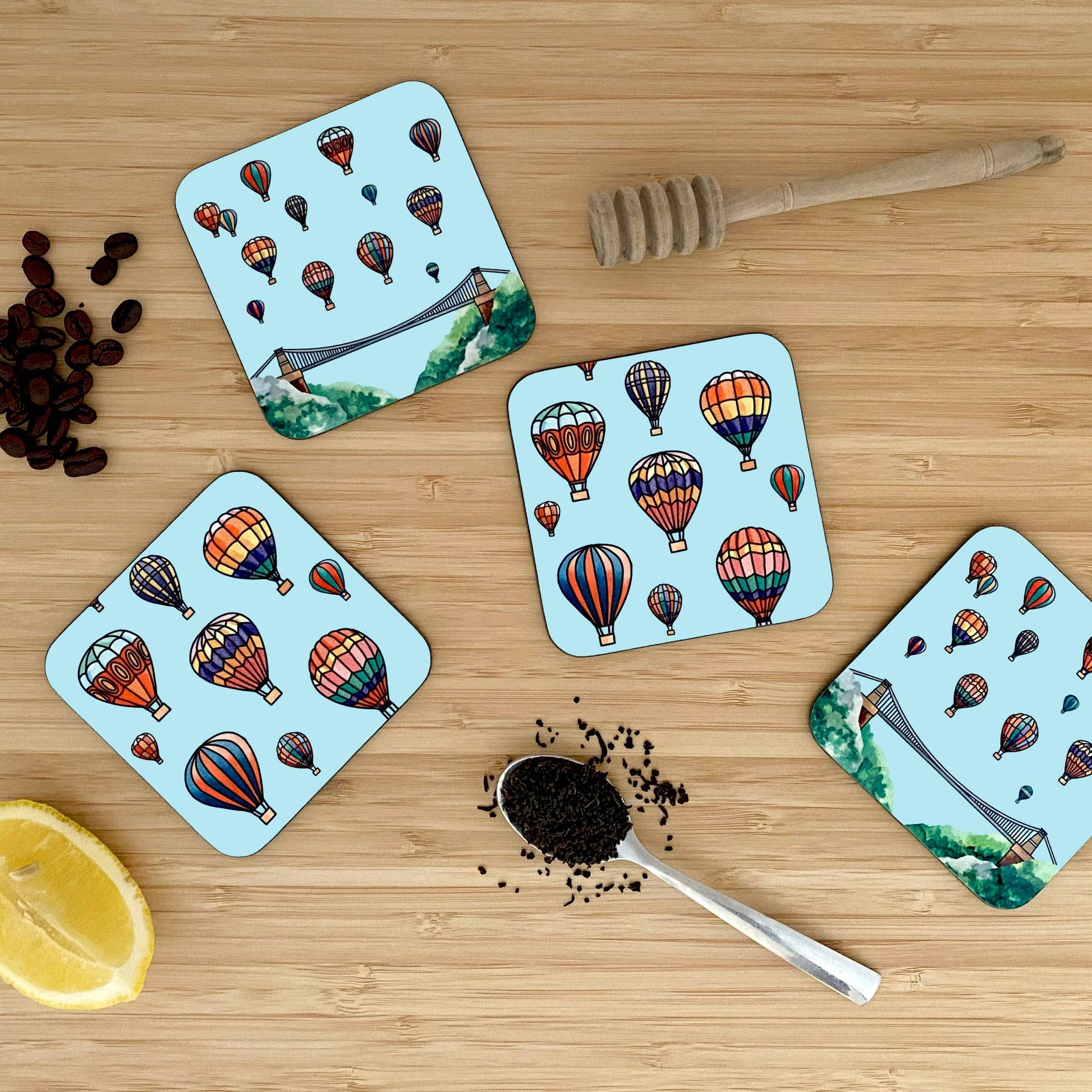 Four coasters with hot air balloon design on a wooden surface with coffee beans and a spoon.