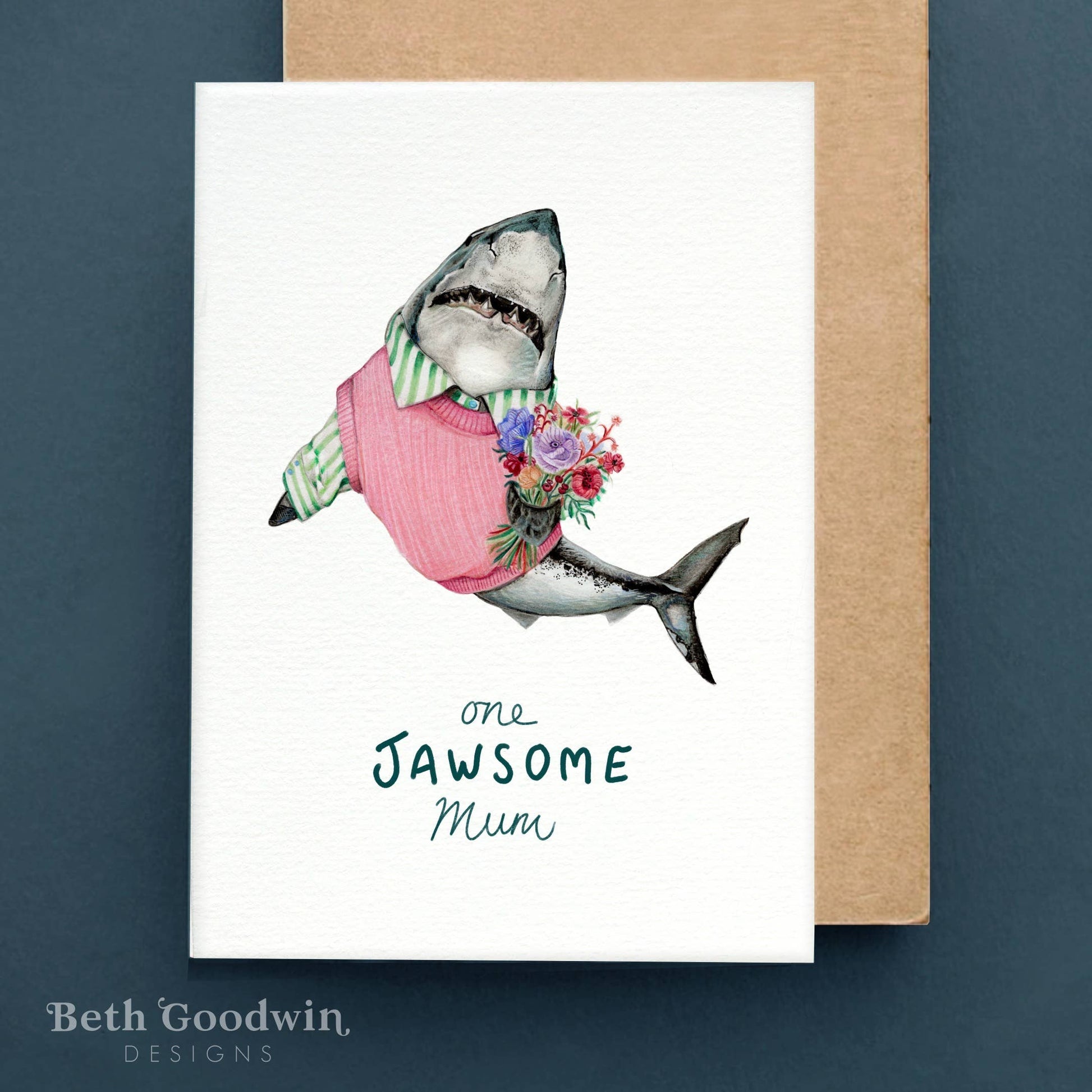 Greeting card with a shark wearing a dress and flowers, text 'one Jawsome Mum', on a white background with a brown envelope.