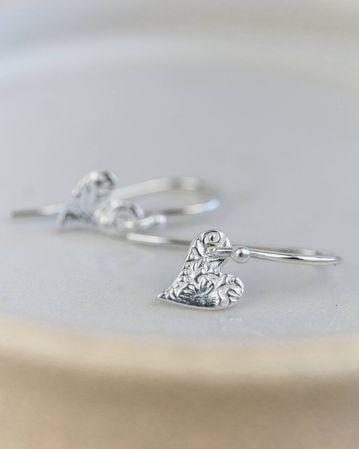 Silver ring with a detailed heart-shaped charm on a light background