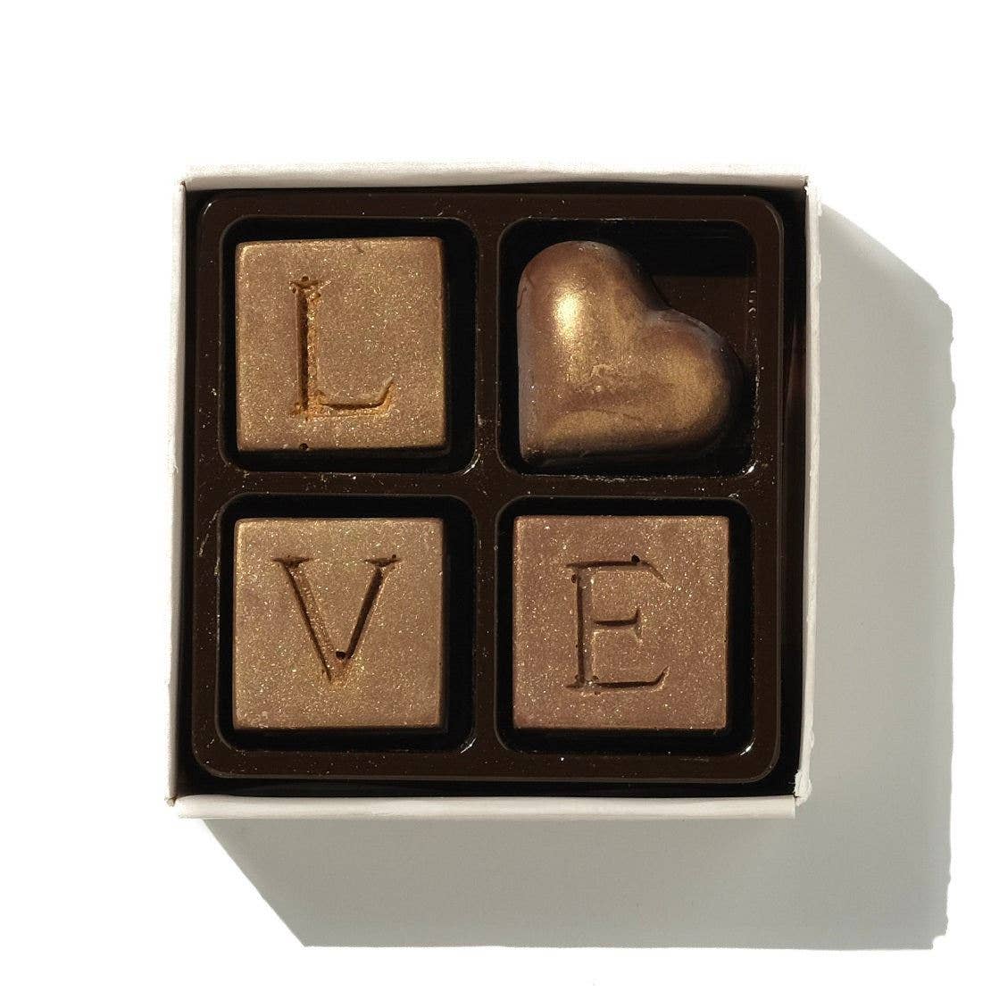 Four chocolate pieces with letters spelling 'LOVE' in a box on a white background