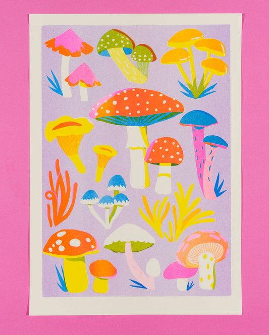 A square art print featuring a colorful collection of whimsical mushrooms in bright yellow, pink, orange, blue, and green on a lavender background, bordered by a white margin and set against a solid pink backdrop.