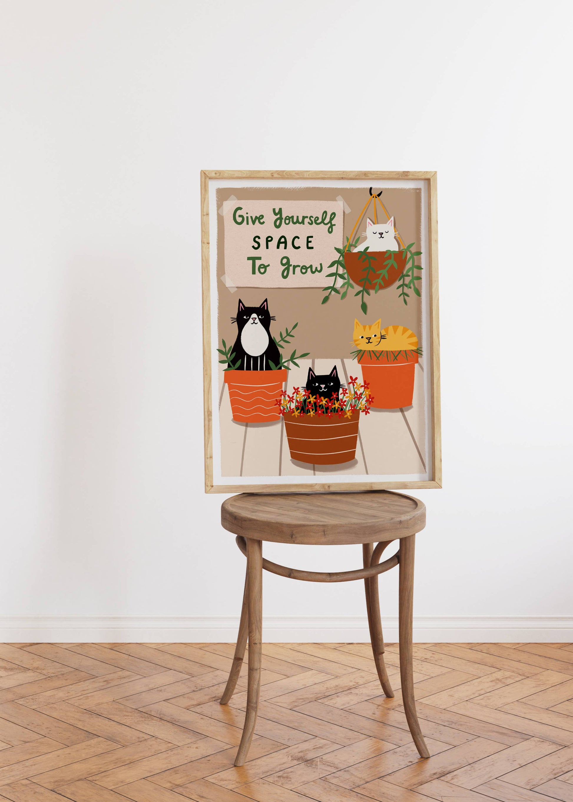Framed artwork with a cat illustration and motivational quote on a wooden stool against a white wall.