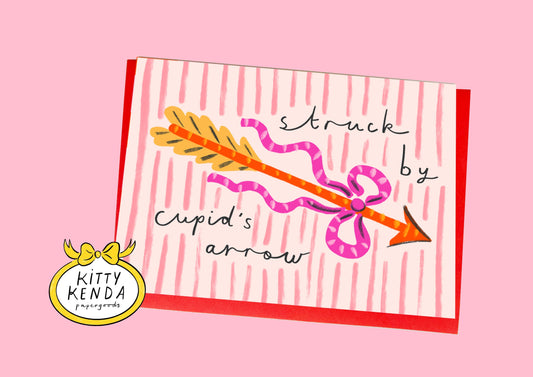 Card with a cartoon arrow and text 'struck by Cupid's arrow' on a pink background, featuring the Kitty Kenda logo.