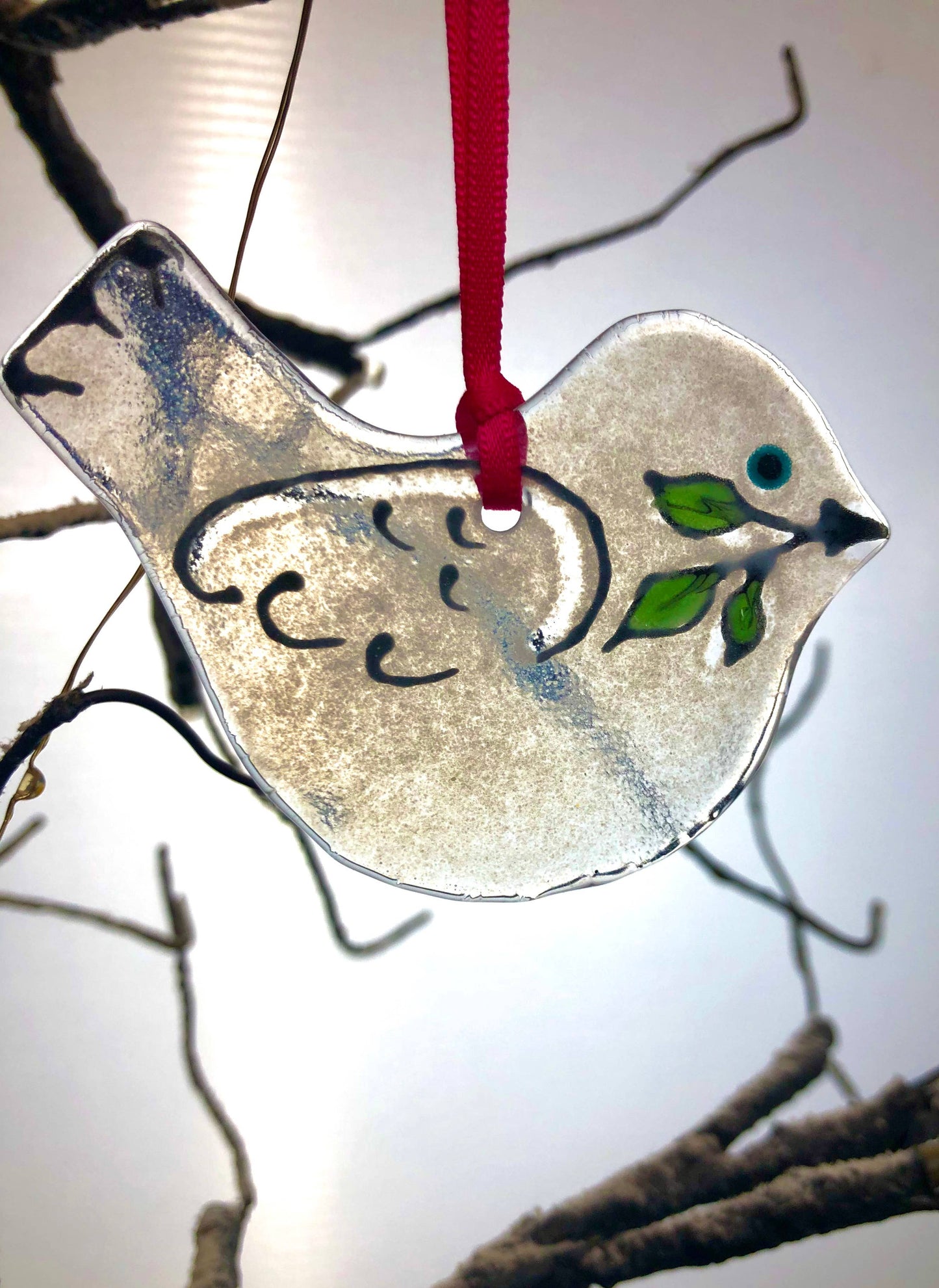 Decorative glass dove ornament hanging on a branch with a red string.