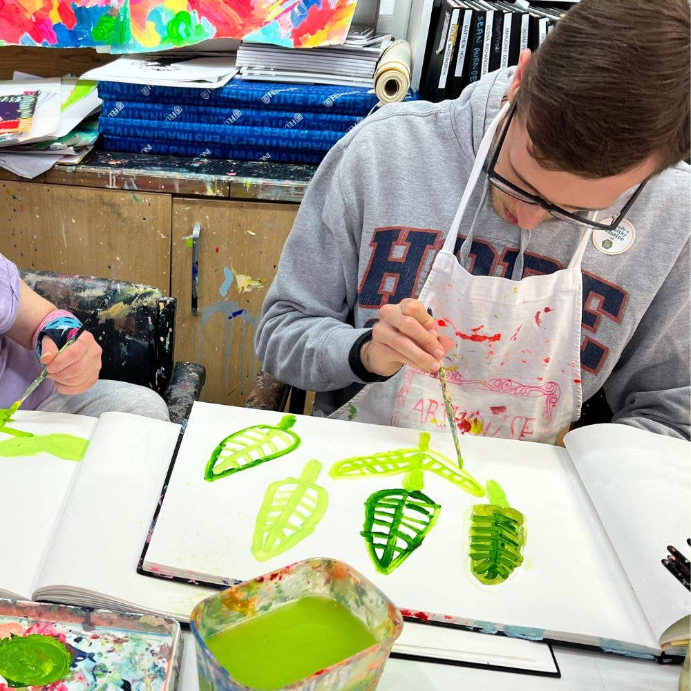 Person painting green leaves on a book with art supplies around