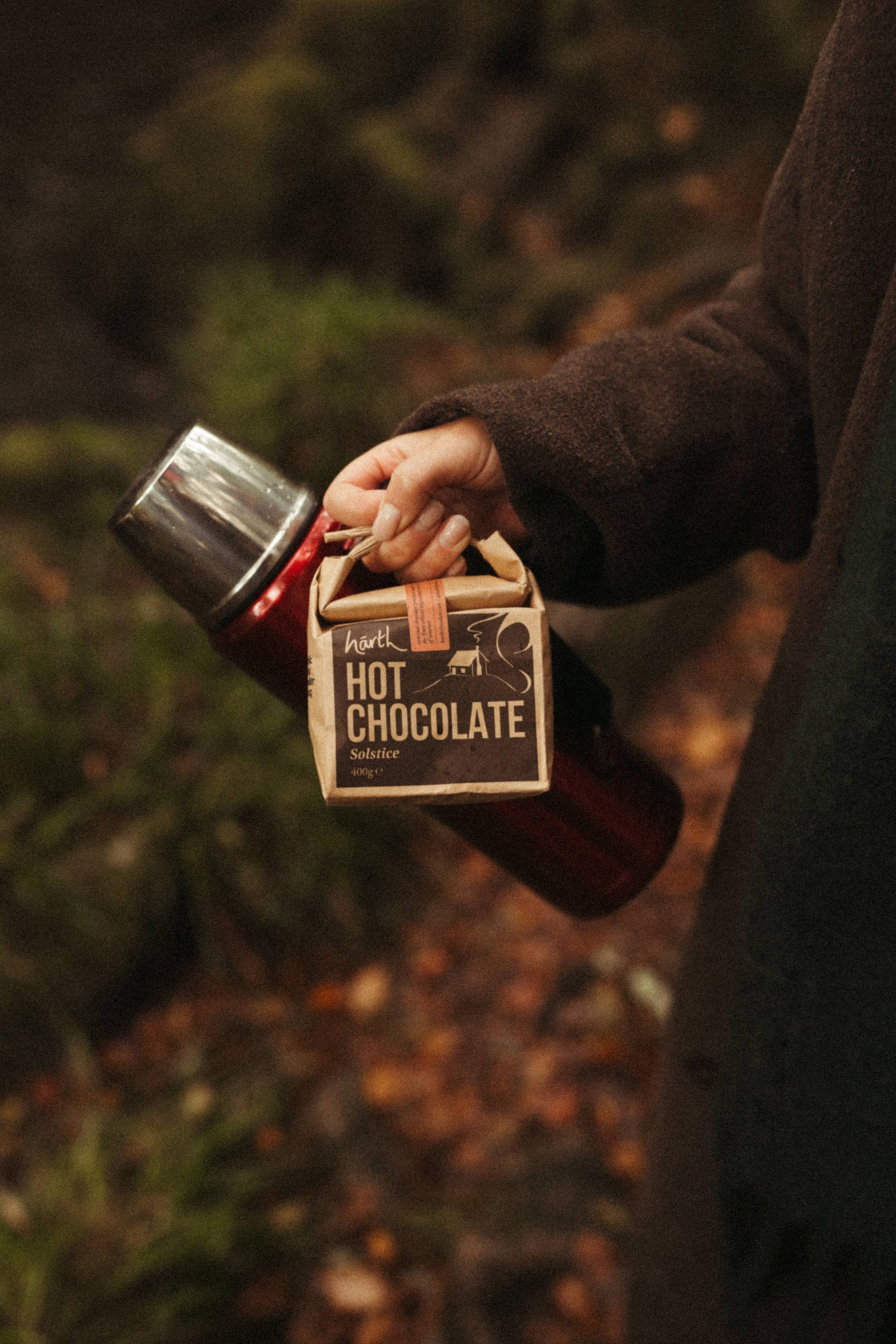 Person holding a container of hot chocolate in a forest setting
