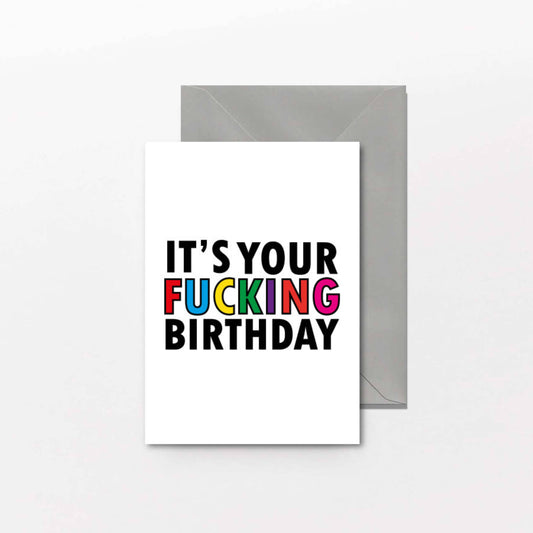 Greeting card with colorful text 'IT'S YOUR FUCKING BIRTHDAY' on a white background with a gray envelope.