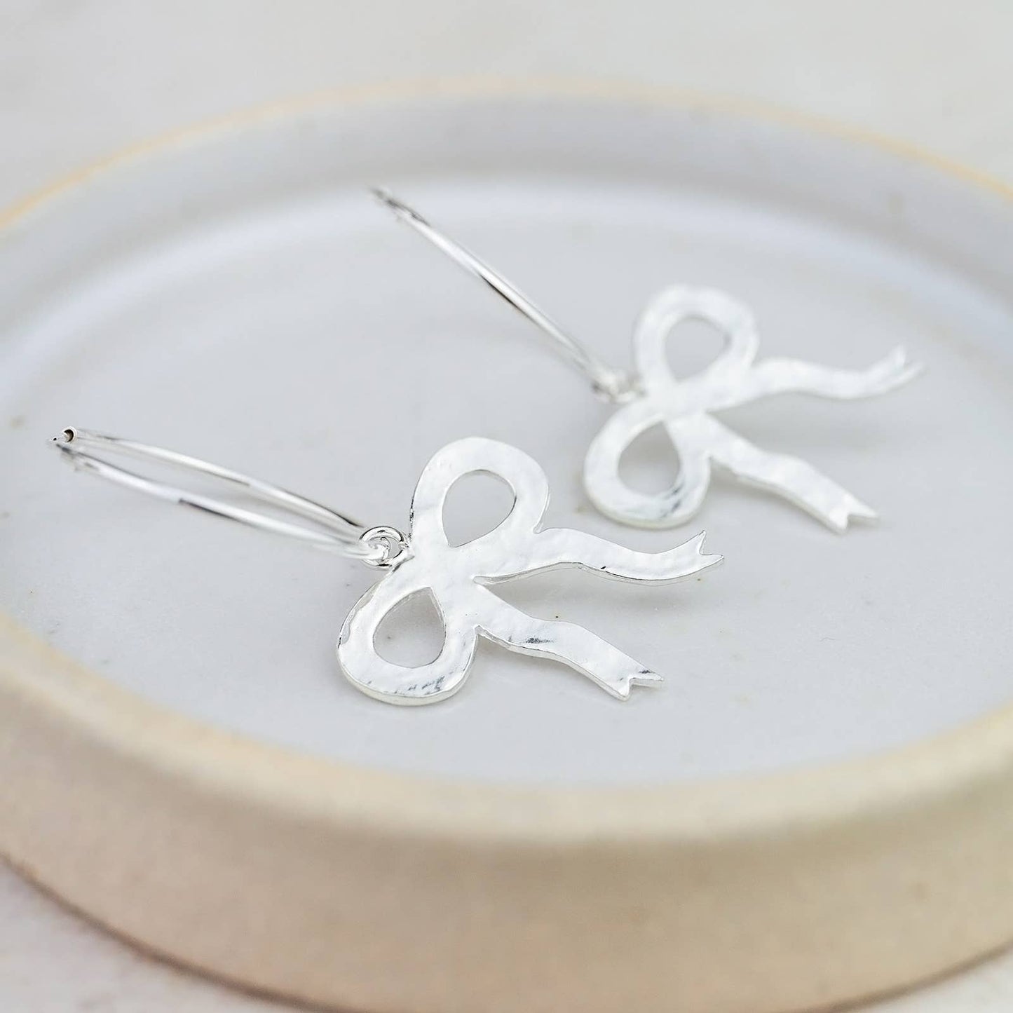Silver bow-shaped earrings on a white plate