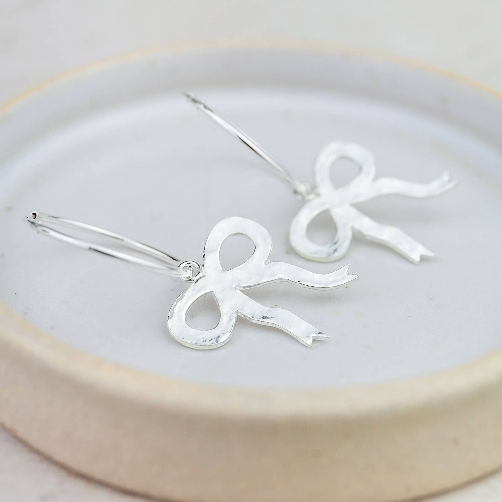Silver bow-shaped earrings on a white plate