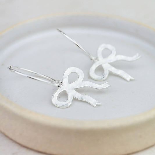 Silver bow-shaped earrings on a white plate