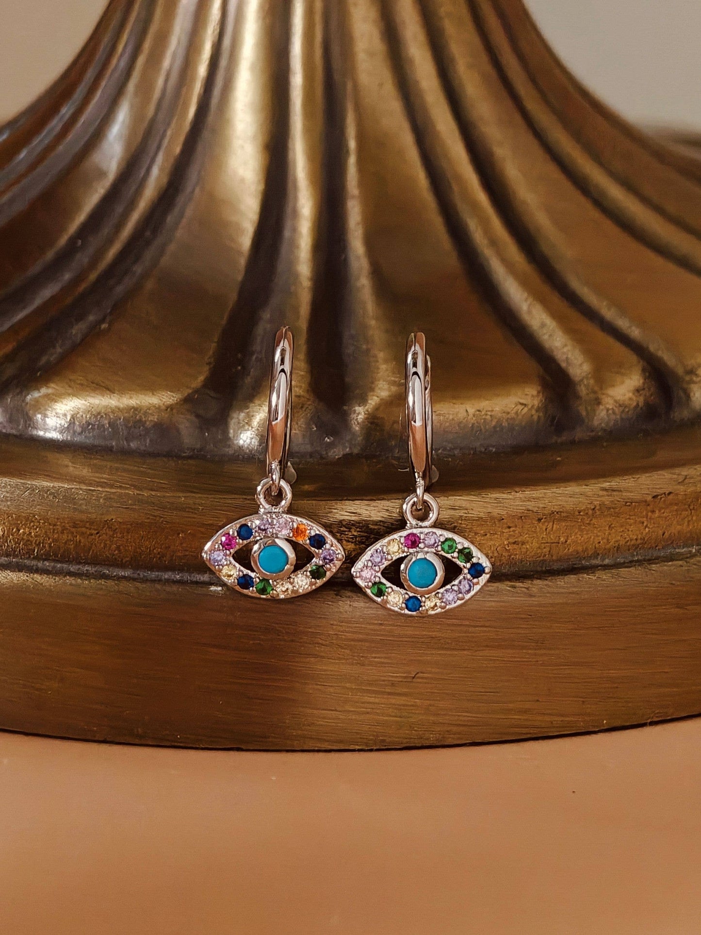 Pair of eye-shaped earrings with colorful gemstones on a decorative stand.