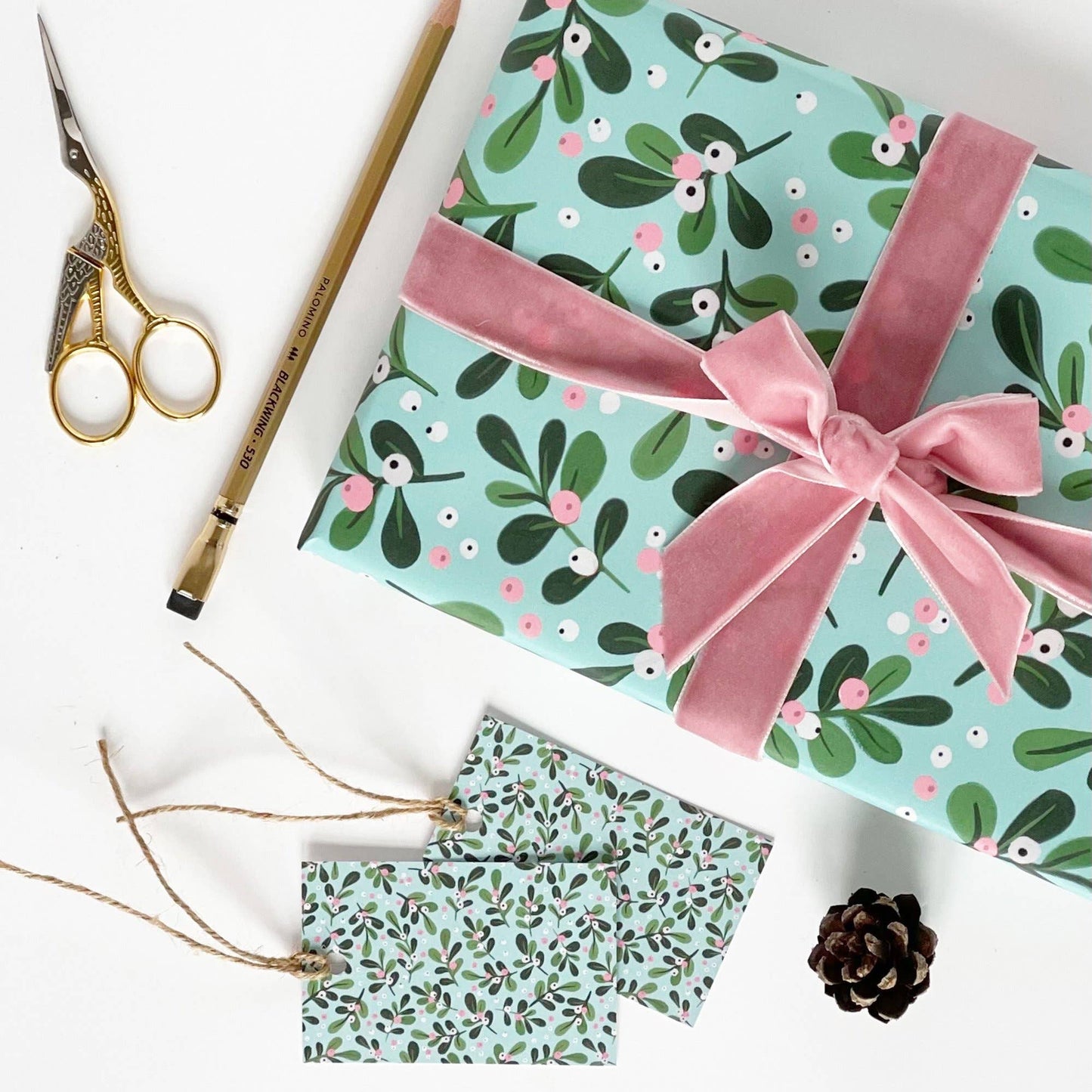 Gift box with floral pattern and pink ribbon, accompanied by matching tags and a pine cone on a white background.