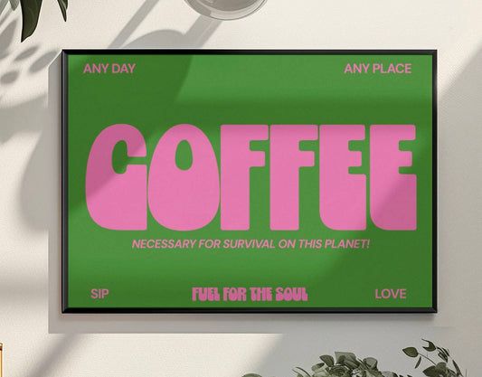 Framed poster with pink 'COFFEE' text on a green background, placed on a light surface with plants around.