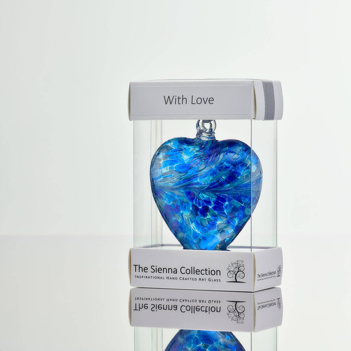 A blue marbled heart-shaped glass ornament displayed inside a clear acrylic presentation box with white branded packaging. The packaging reads 'With Love' on top and 'The Sienna Collection' on the bottom.