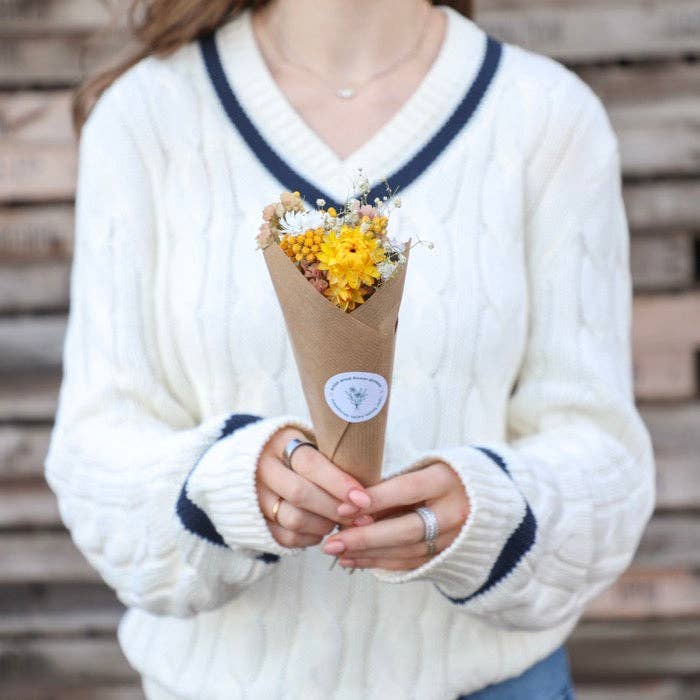 Person holding a bouquet of yellow flowers wrapped in brown paper against a wooden background