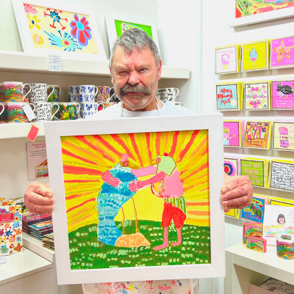 Man holding a framed colorful artwork in a store with shelves of products.
