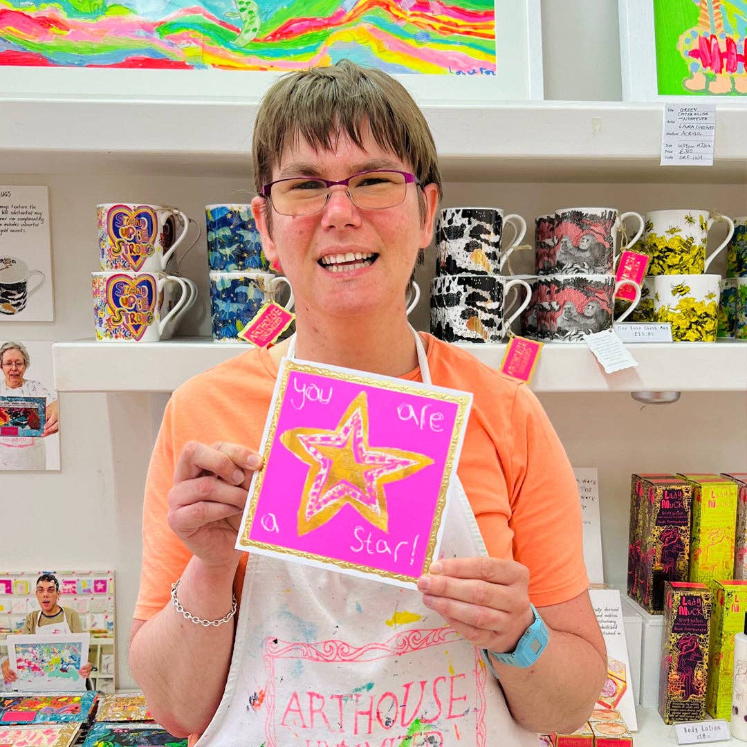 Person holding a card with a star design in a store setting with various items on shelves.
