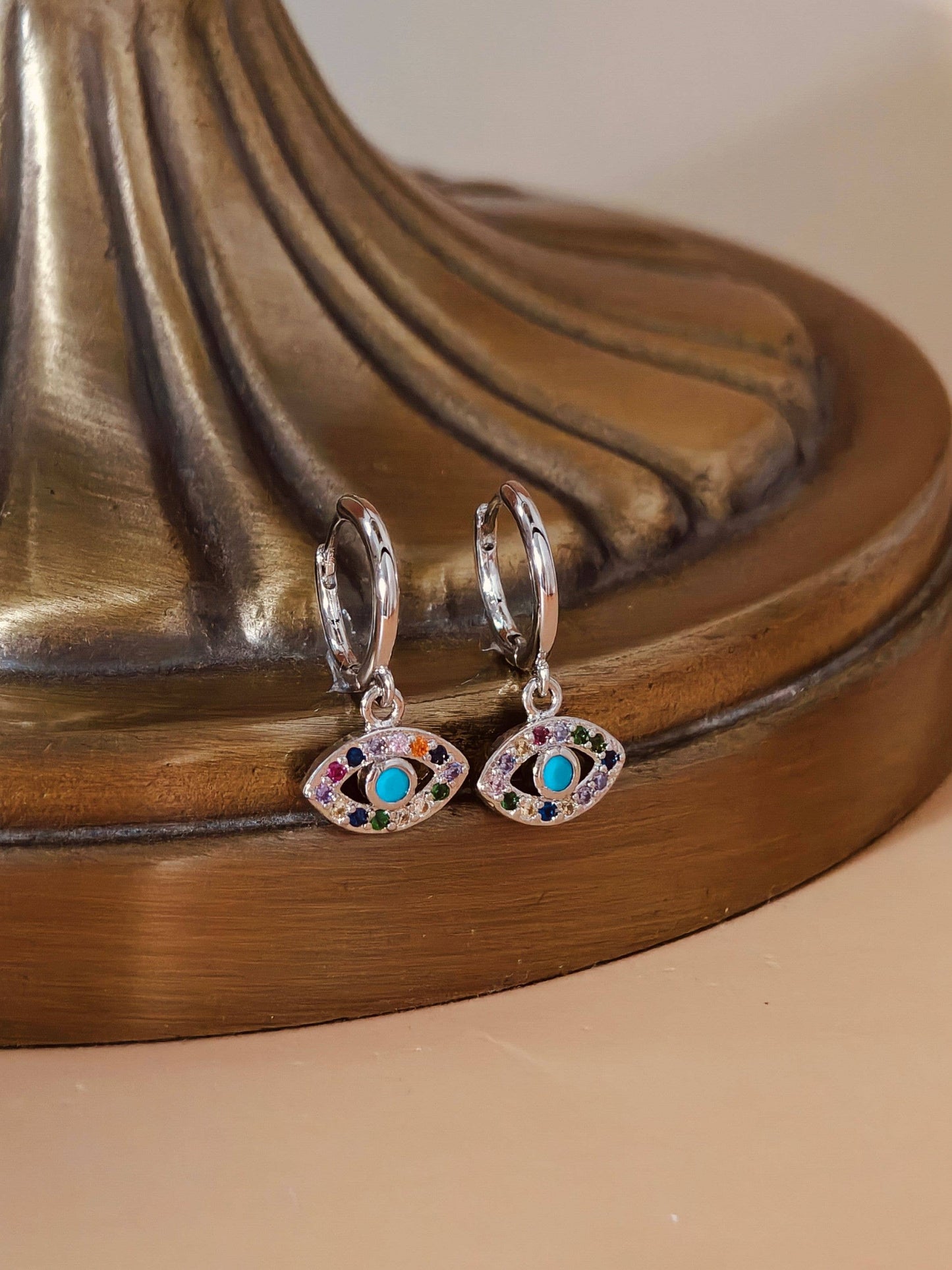 Pair of silver earrings with eye design on a bronze surface