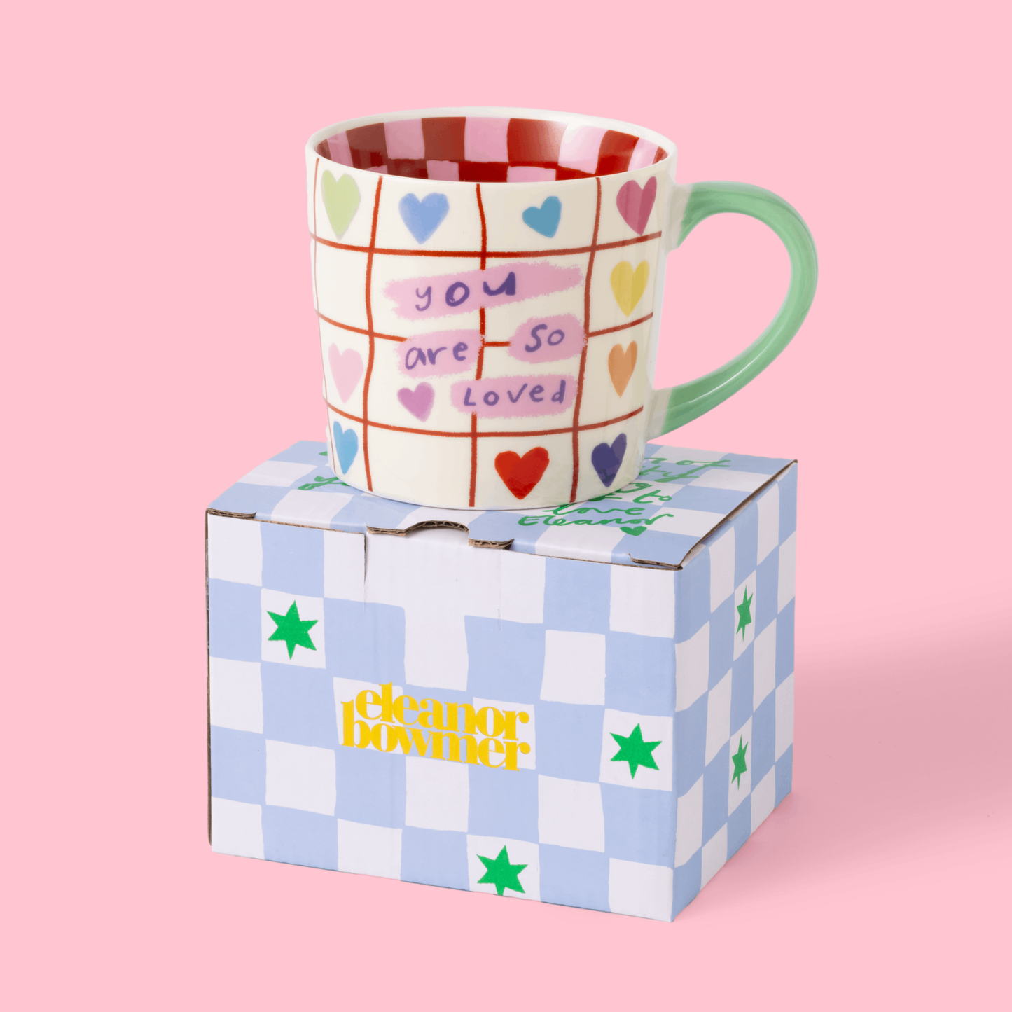 Mug with colorful text and patterns on a checkered box against a pink background