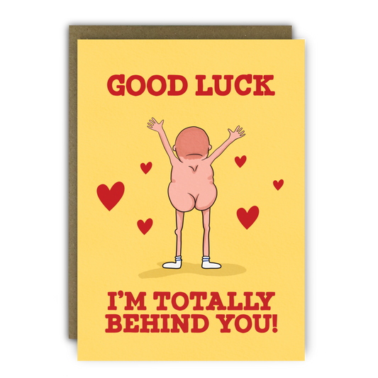 A yellow card with red text that says "Good Luck - I'm Totally Behind You!" with a cartoon drawing of a naked man facing away from us in just his socks. There are cartoon hearts around him.