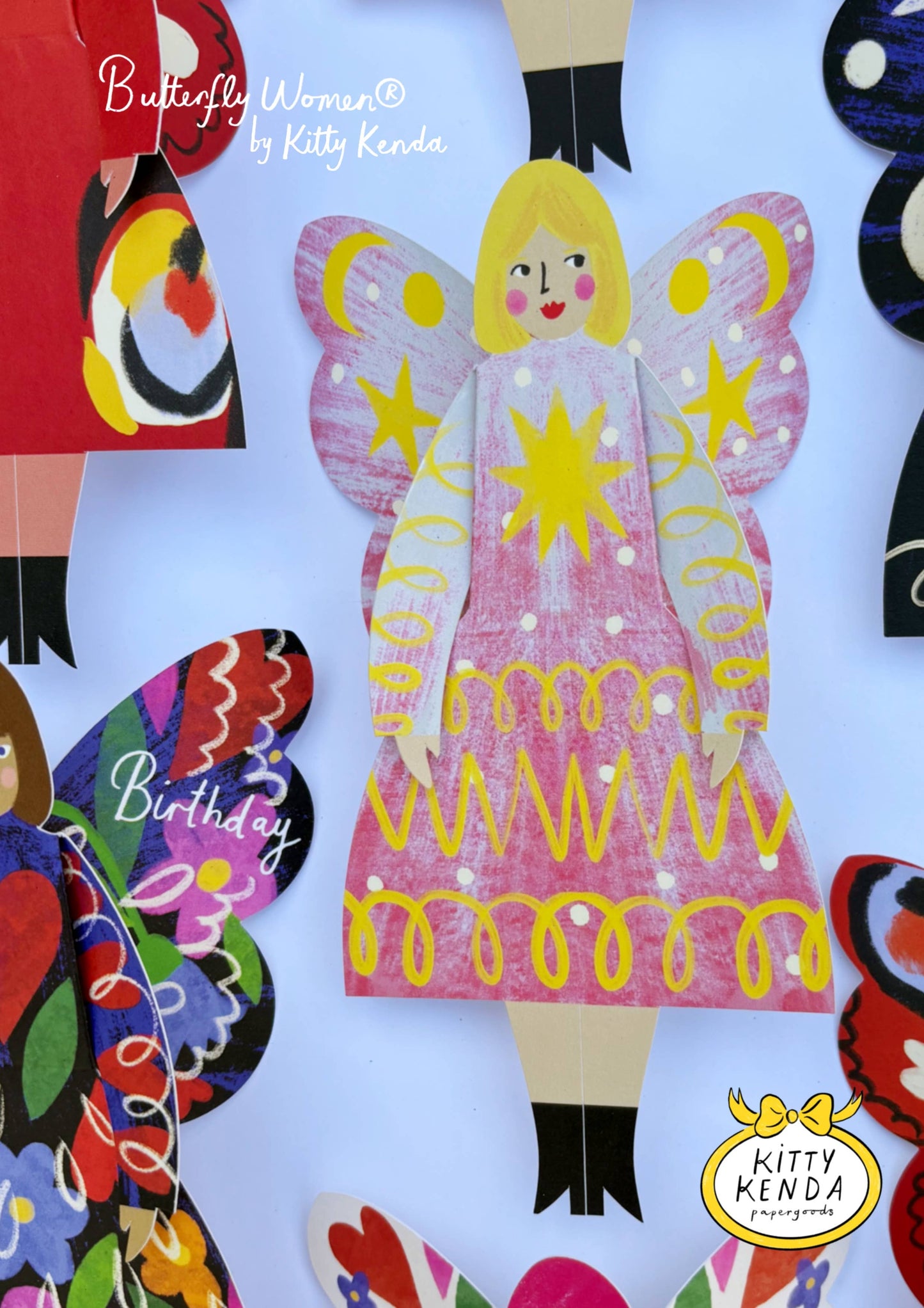 Colorful paper cutout of a butterfly woman with a pink dress and yellow accents, surrounded by other decorative elements.