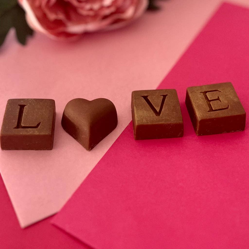 Chocolate letters spelling 'LOVE' on a pink background with a heart-shaped chocolate piece.