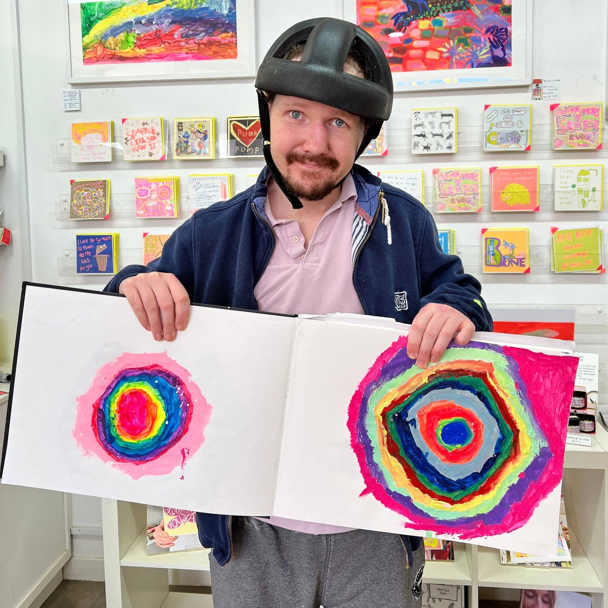 Person holding a book with colorful circular artwork in an art gallery setting