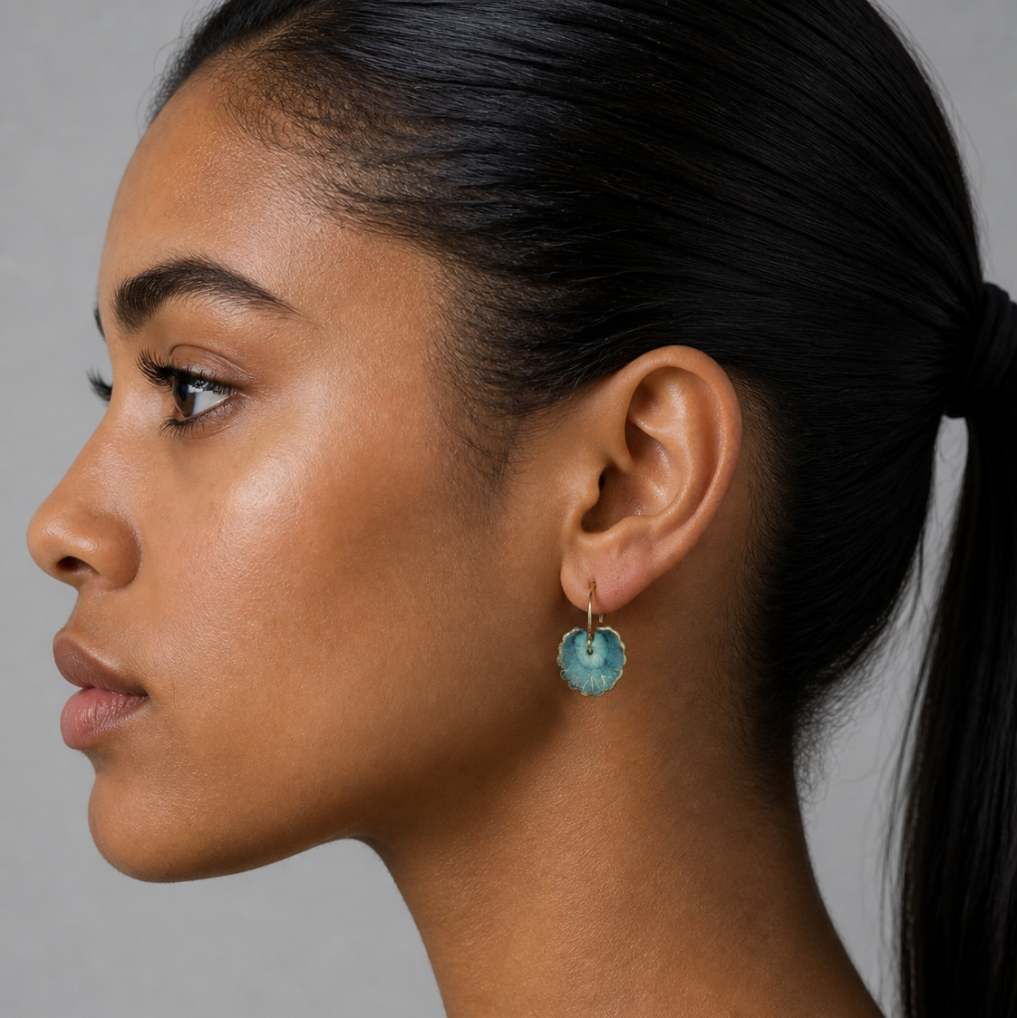 Close-up of a woman wearing a blue heart-shaped earring against a gray background