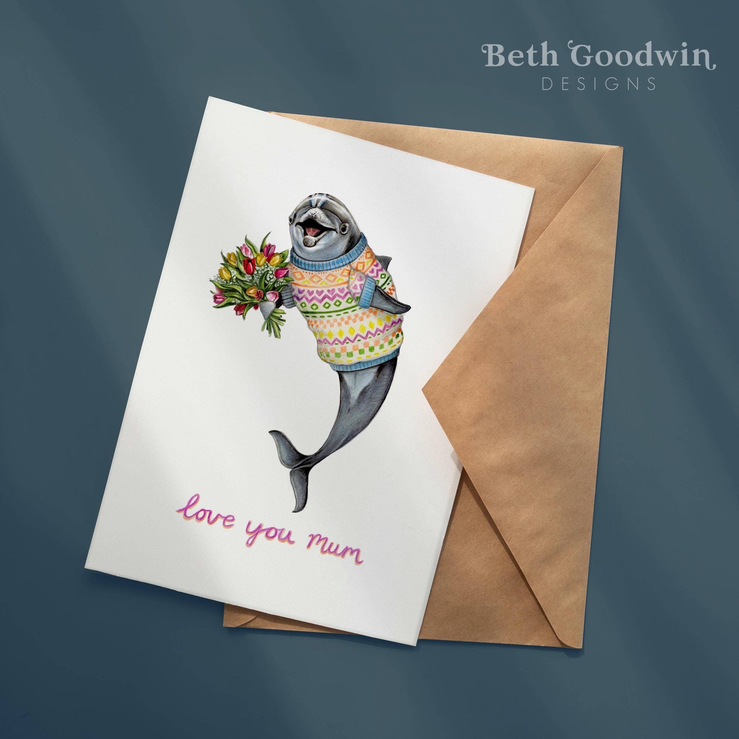 Greeting card with a seal wearing a sweater and holding flowers, accompanied by an envelope on a dark blue background.