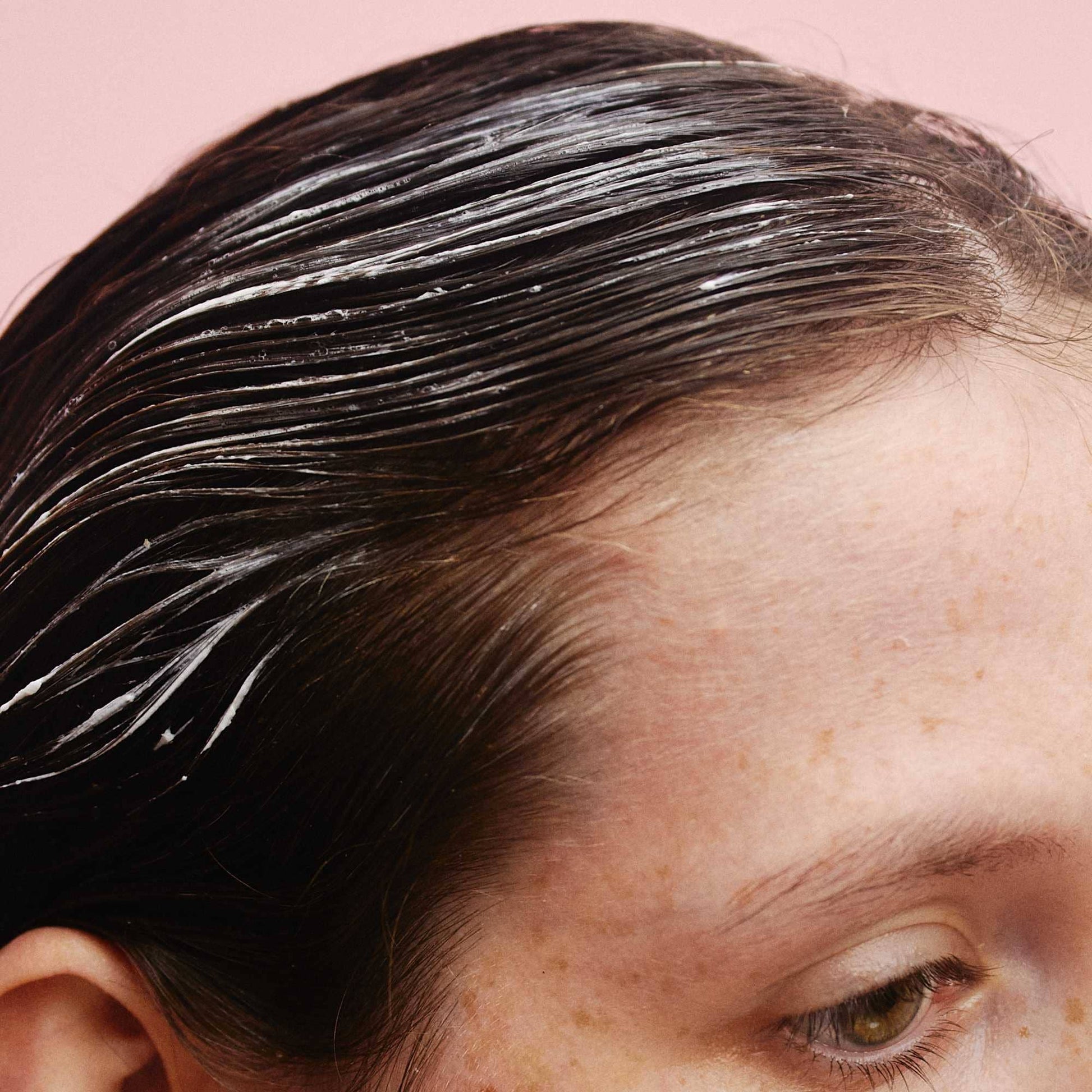 Person with black hair applying a product to their scalp against a pink background