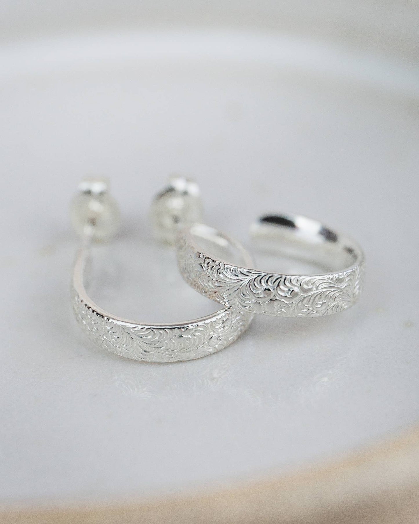 Silver hoop earrings with intricate designs on a light background