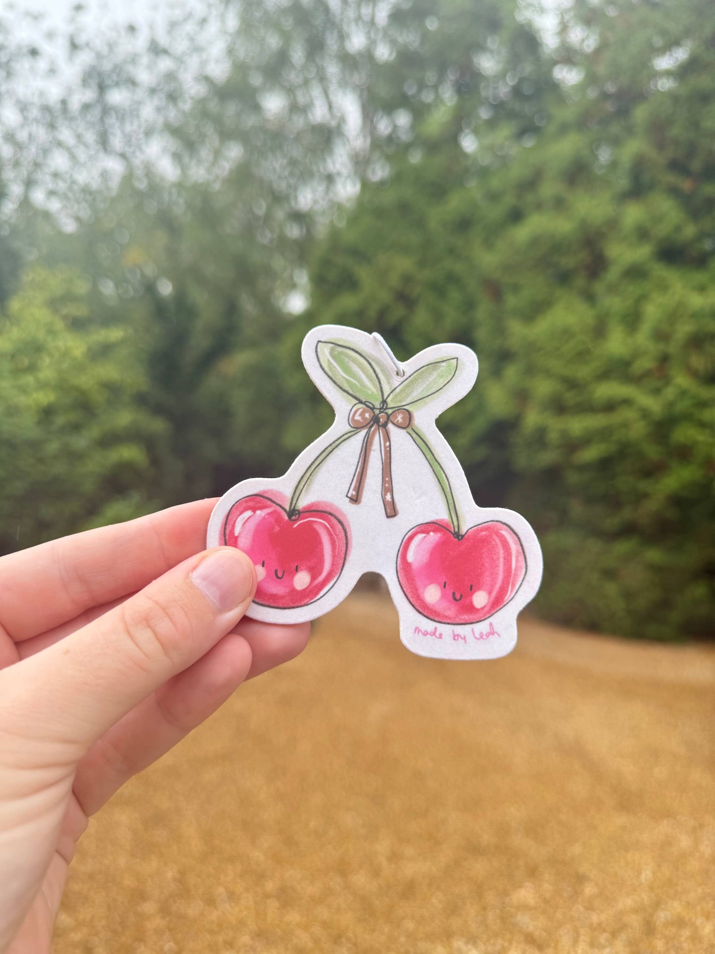 Hand holding a sticker with cartoon cherries against a blurred natural background