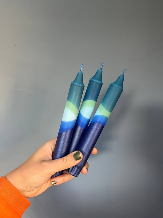 Hand holding three blue and green gradient candles against a gray background