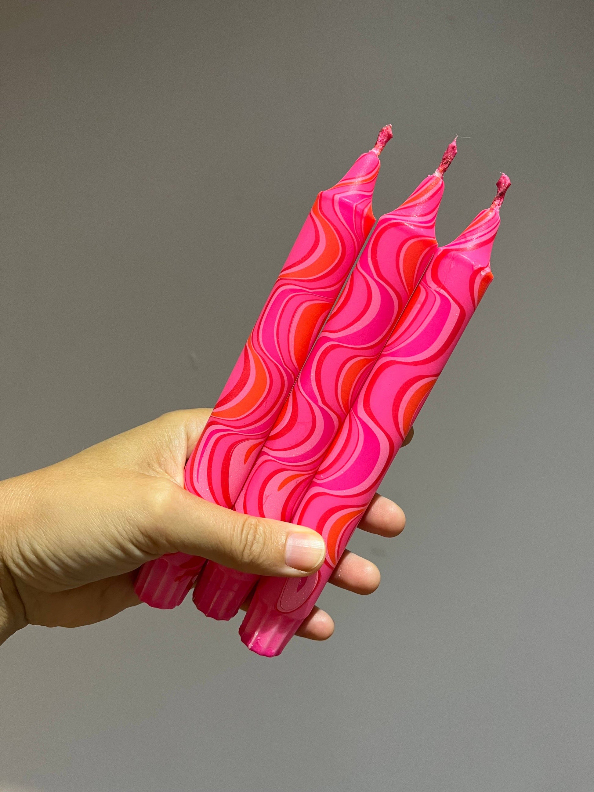 Hand holding pink wavy-patterned candles against a gray background