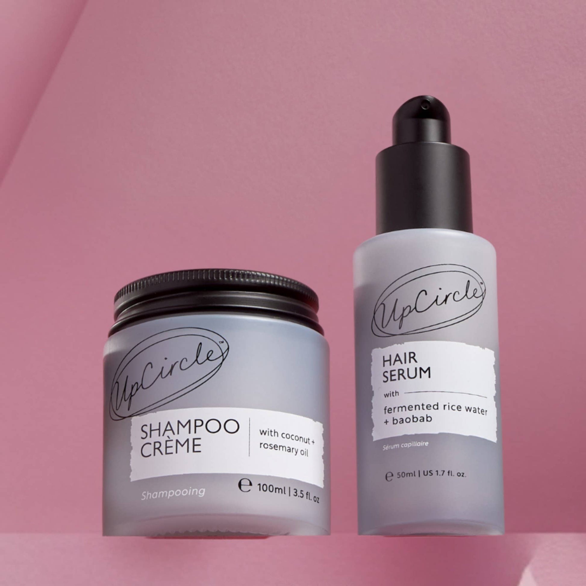 UpCircle shampoo crème jar and hair serum bottle on a pink background